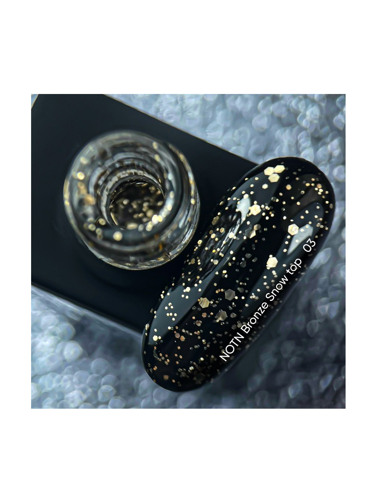 Top hybrydowy Bronze Snow NAILSOFTHENIGHT z nieregularnymi miedzianymi cząsteczkami na tle butelki